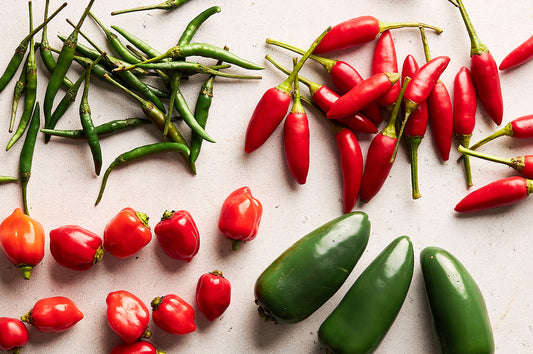 Assorted chillies in red and green, including jalapeños, bird’s eye, and habaneros, arranged on a light background.