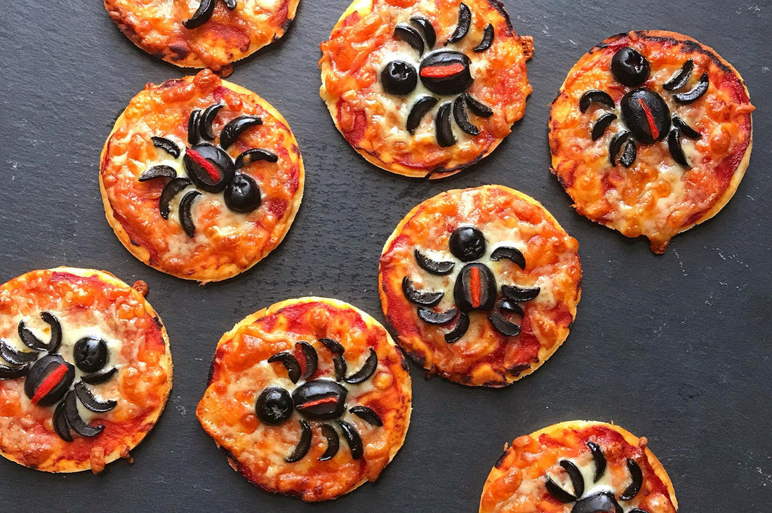 Mini pizzas topped with black olive spiders on a dark serving board.