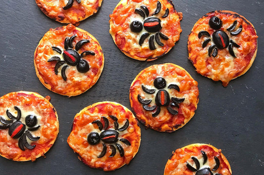 Mini pizzas topped with black olive spiders on a dark serving board.