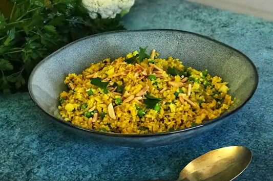 Spiced cauliflower rice with peas, herbs, and almonds served in a grey bowl.