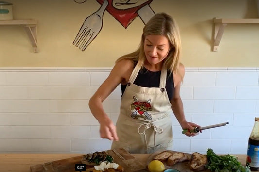Sophie from The Dinner Ladies  preparing vegie-packed breakfast bruschetta with fresh herbs and bread on a bench.