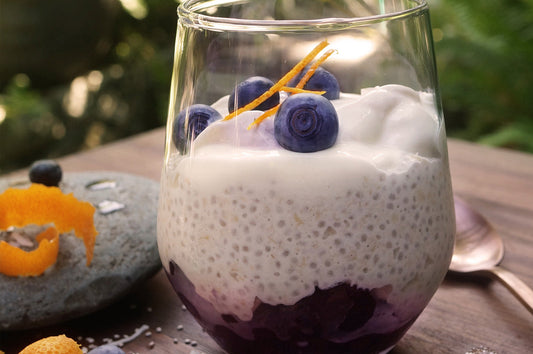 Glass of coconut and blueberry bircher muesli topped with yoghurt, berries, and zest.
