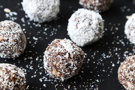 Chocolate-coconut bliss balls coated in shredded coconut on a dark surface.