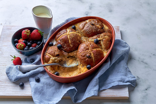 Hot cross bread and butter pudding baked golden in a dish with berries on the side.