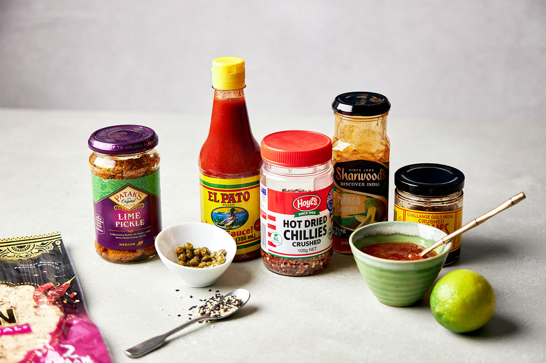 Pantry staples including sauces, spices, lime, and condiments displayed with a bowl and spoon, ready to enhance Dinner Ladies meals.