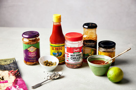 Pantry staples including sauces, spices, lime, and condiments displayed with a bowl and spoon, ready to enhance Dinner Ladies meals.