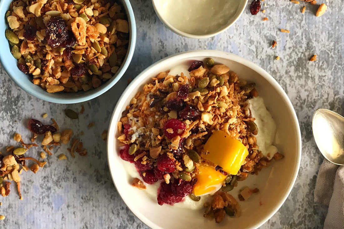 Bowl of paleo granola with nuts, seeds, dried fruit, and fresh mango chunks.