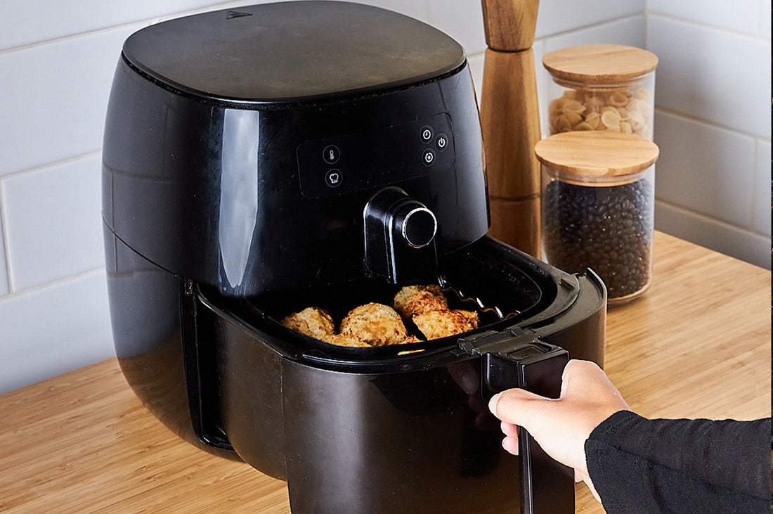 Black air fryer on a kitchen bench with golden food cooking inside the open tray.
