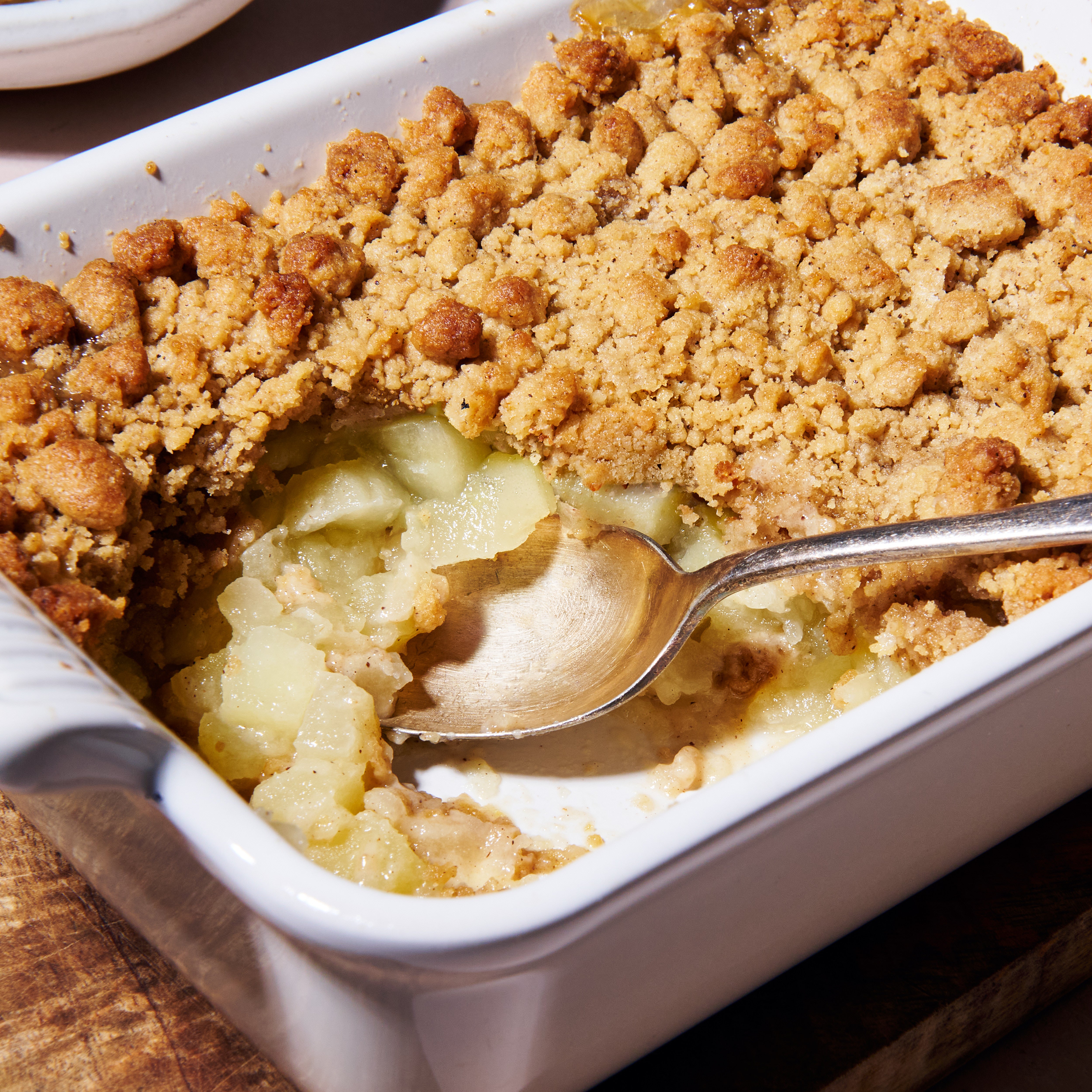 Close up of the apple and gingerbread crumble with a spoon scooping through the golden crumble topping into soft stewed apple beneath