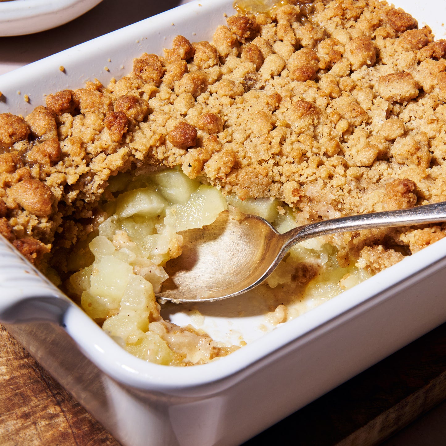 Close up of the apple and gingerbread crumble with a spoon scooping through the golden crumble topping into soft stewed apple beneath