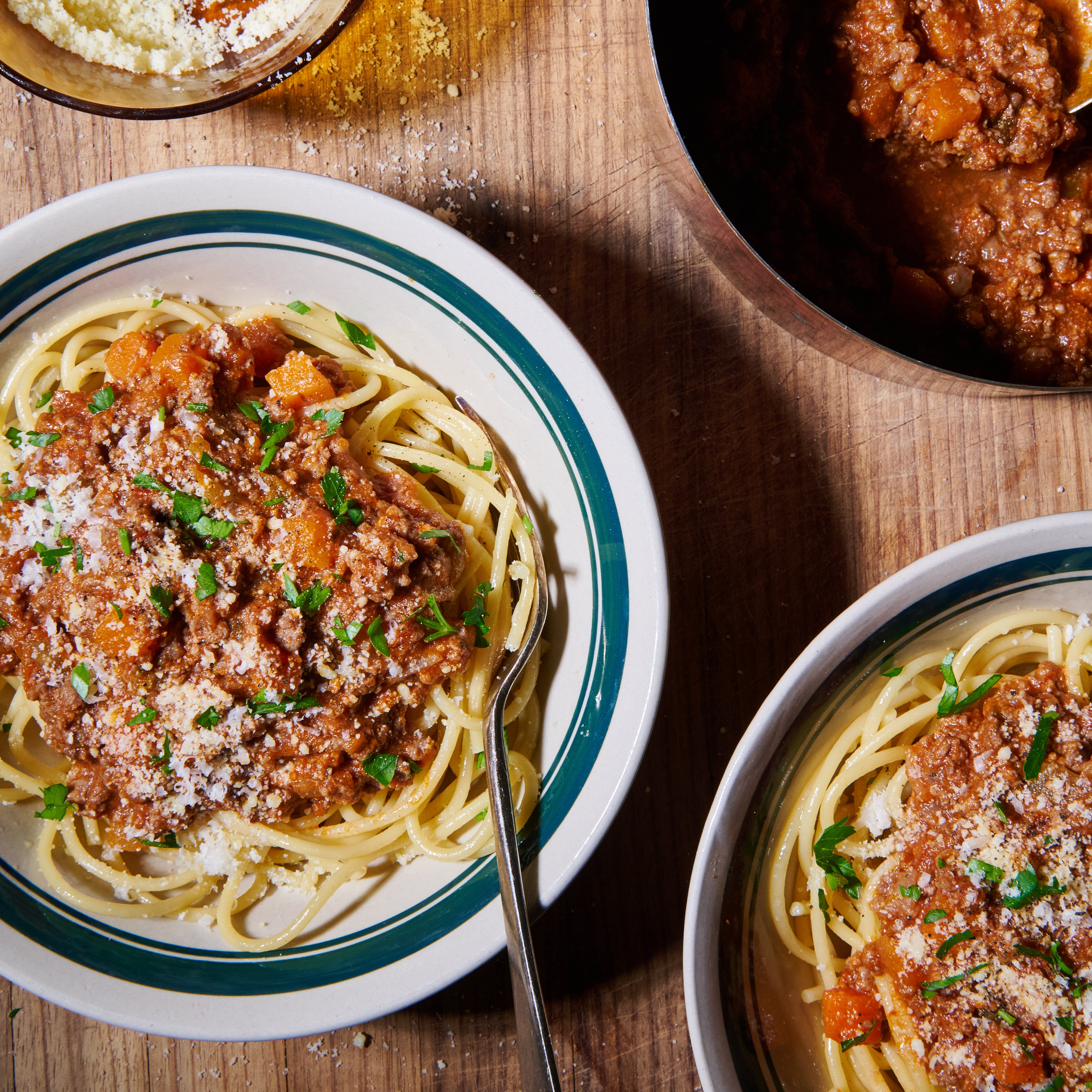 Two bowls of beef bolognese served over spaghetti, garnished with parsley and grated parmesan