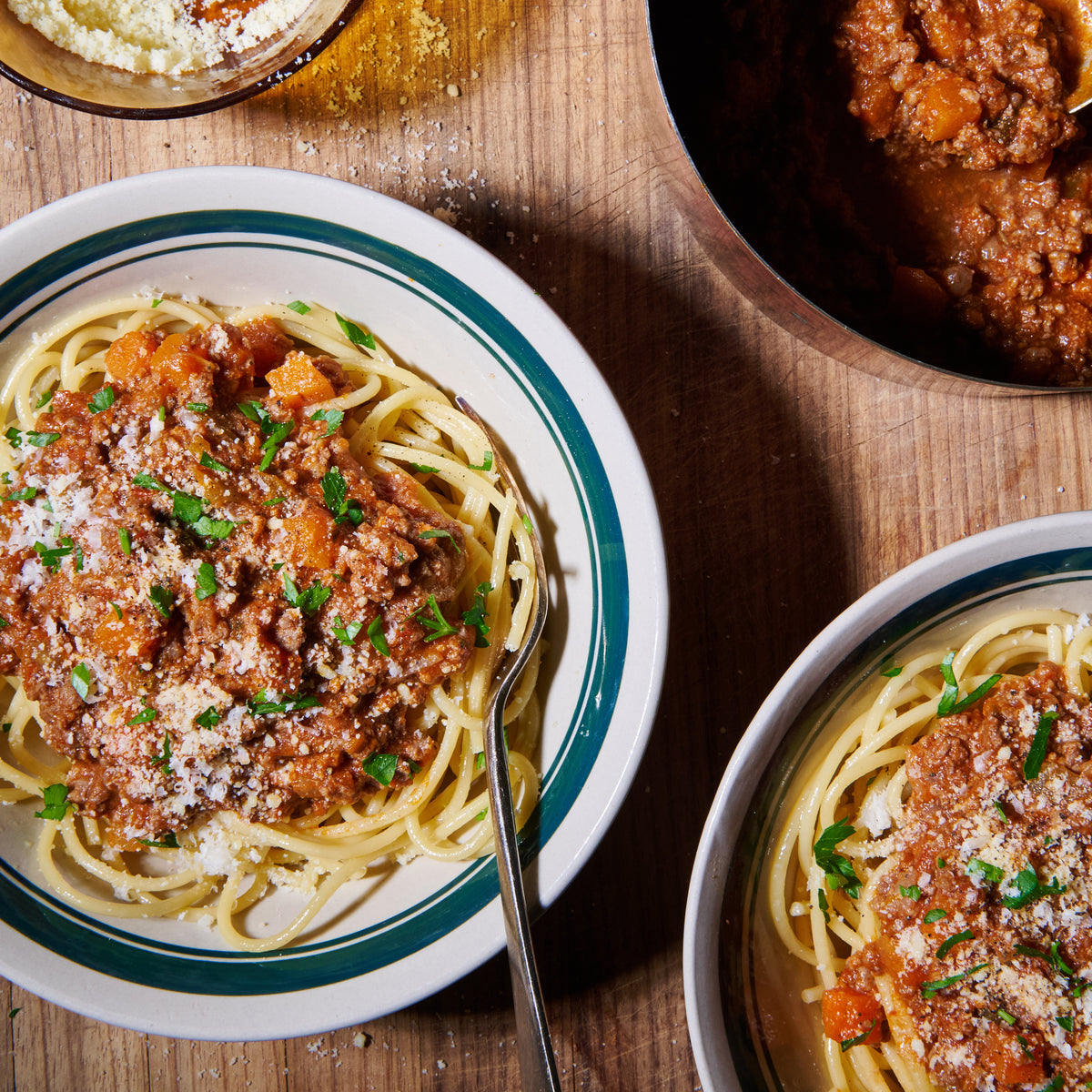 Two bowls of beef bolognese served over spaghetti, garnished with parsley and grated parmesan