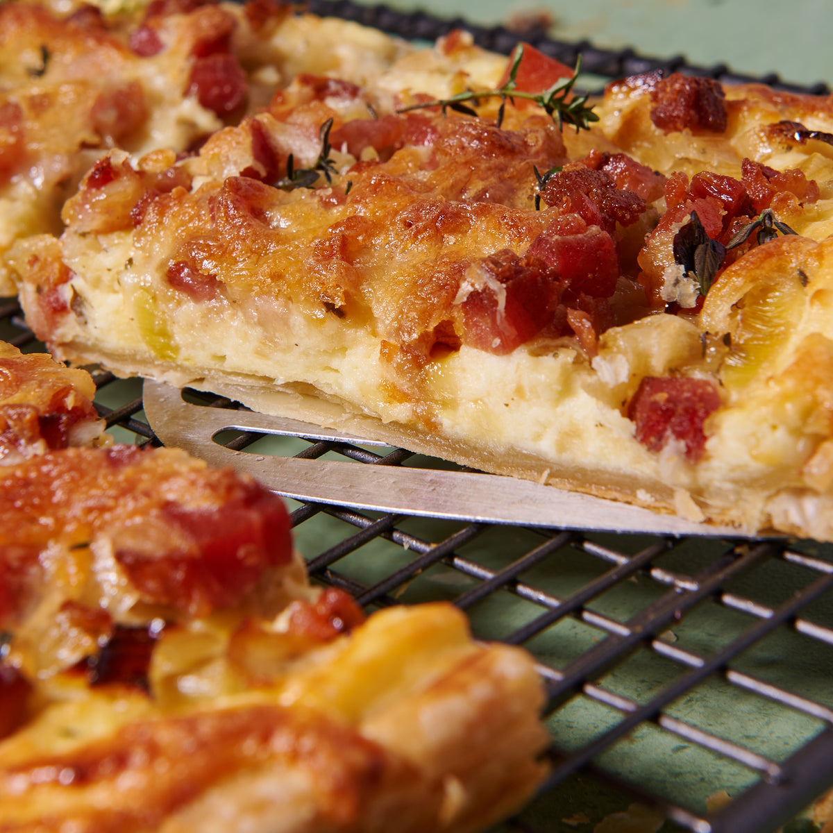 Close-up of a slice of bacon, leek and ricotta tart being lifted, showing the flaky pastry base, crispy bacon bits and creamy ricotta filling