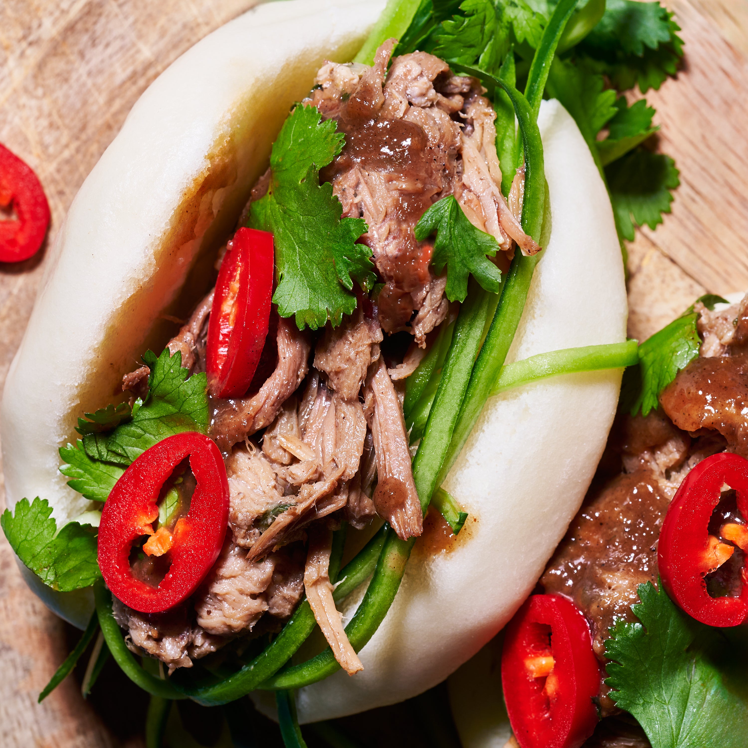 Close-up of bao bun stuffed with slow-cooked hoisin pork, cucumber, coriander, and sliced red chilli.