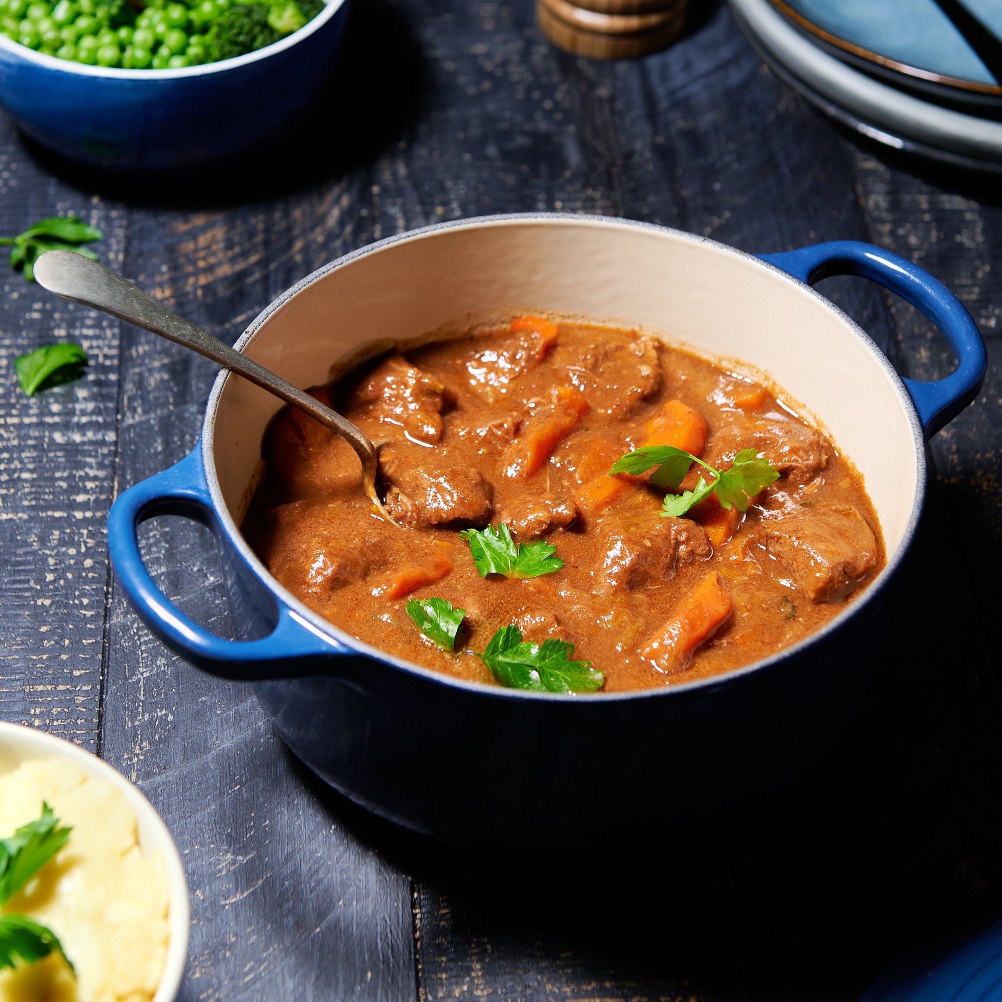 Beef and carrot stew in a rich brown gravy, served in a blue enamel pot with a spoon and garnished with parsley