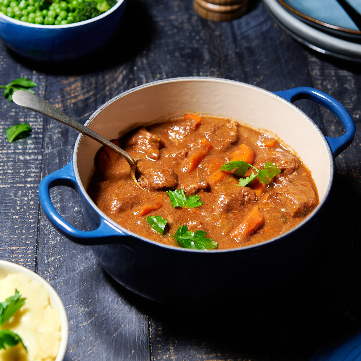 Beef and carrot stew in a rich brown gravy, served in a blue enamel pot with a spoon and garnished with parsley