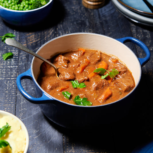 Beef and carrot stew in a rich brown gravy, served in a blue enamel pot with a spoon and garnished with parsley