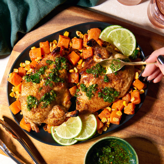 Chicken chimichurri traybake with roasted sweet potato and corn, drizzled with green chimichurri and served with lime wedges