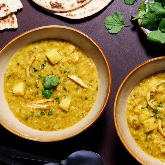 Overhead view of two bowls of Chicken Mulligatawny Soup with flatbreads and fresh coriander on a dark table.