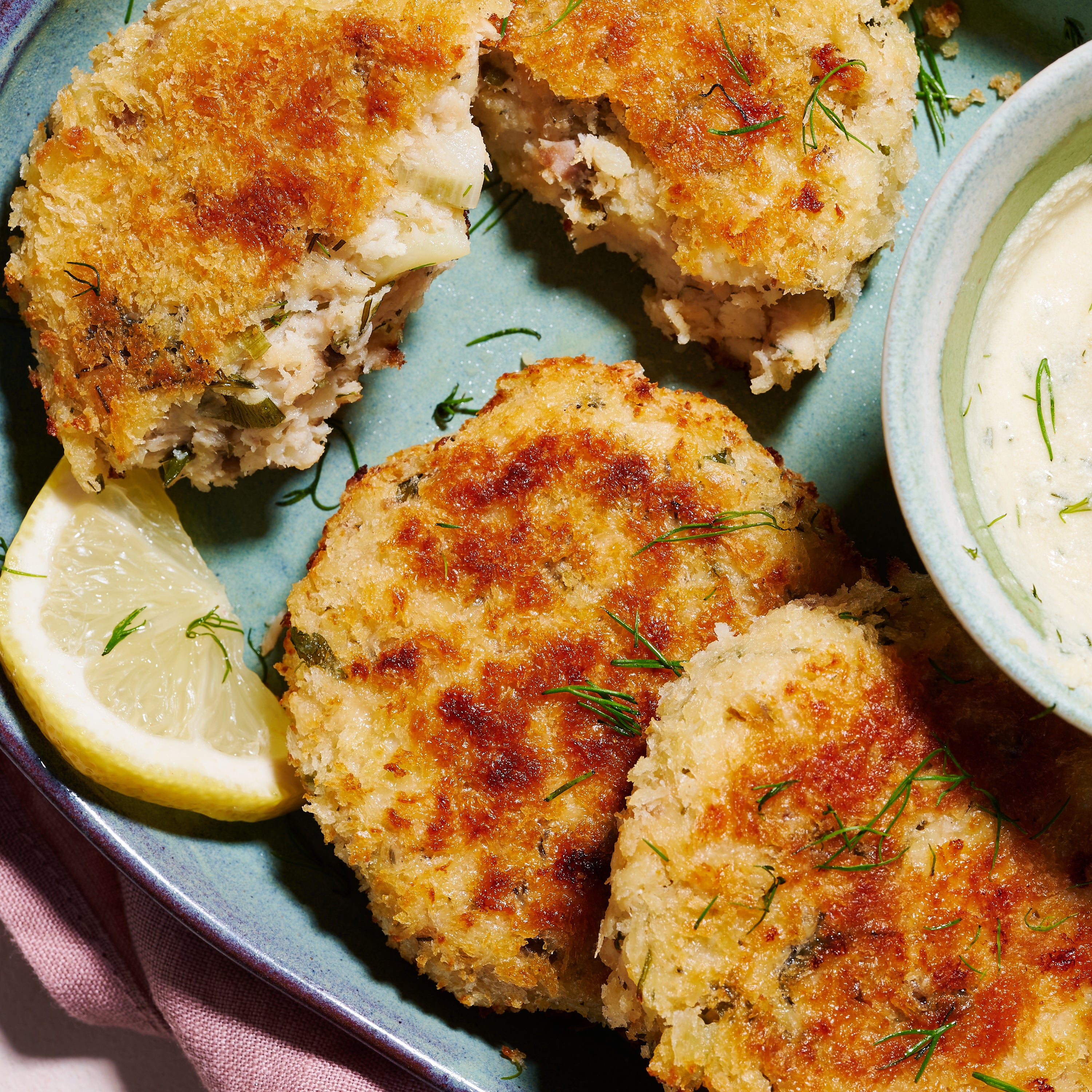 Close-up of Salmon & Barramundi Fish Cakes showing crisp panko crust, herby filling, and lemon wedge garnish.