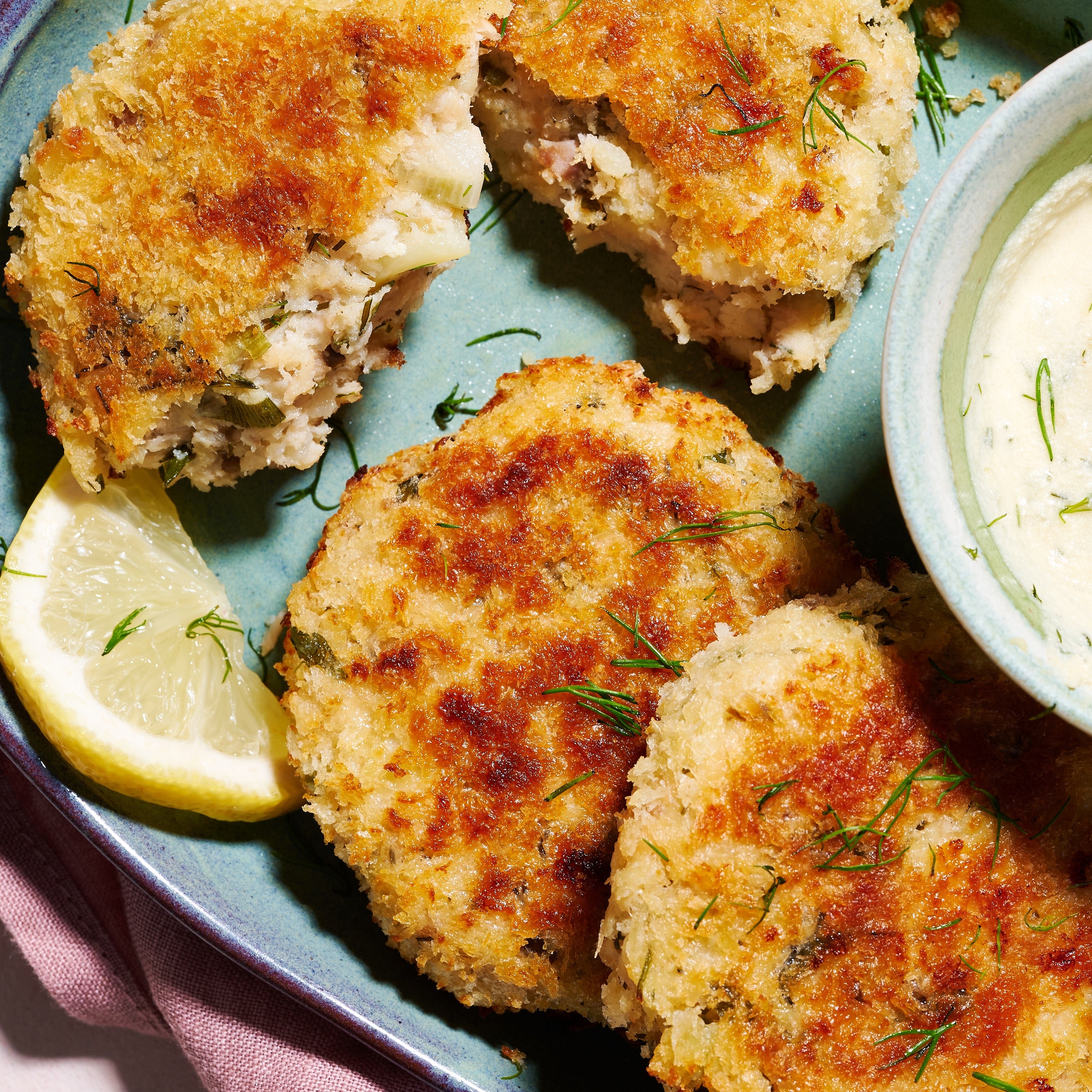 Close-up of Salmon & Barramundi Fish Cakes showing crisp panko crust, herby filling, and lemon wedge garnish.