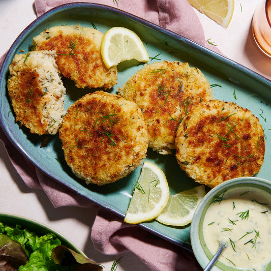 Plate of golden Salmon & Barramundi Fish Cakes with lemon wedges, fresh dill, and a creamy dipping sauce.
