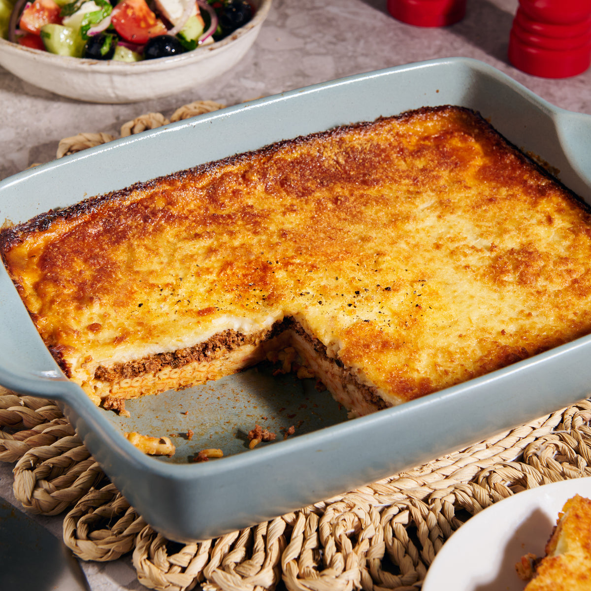 Lamb pastitsio with fetta in a baking dish, showing layers of macaroni, spiced lamb and a golden baked bechamel topping