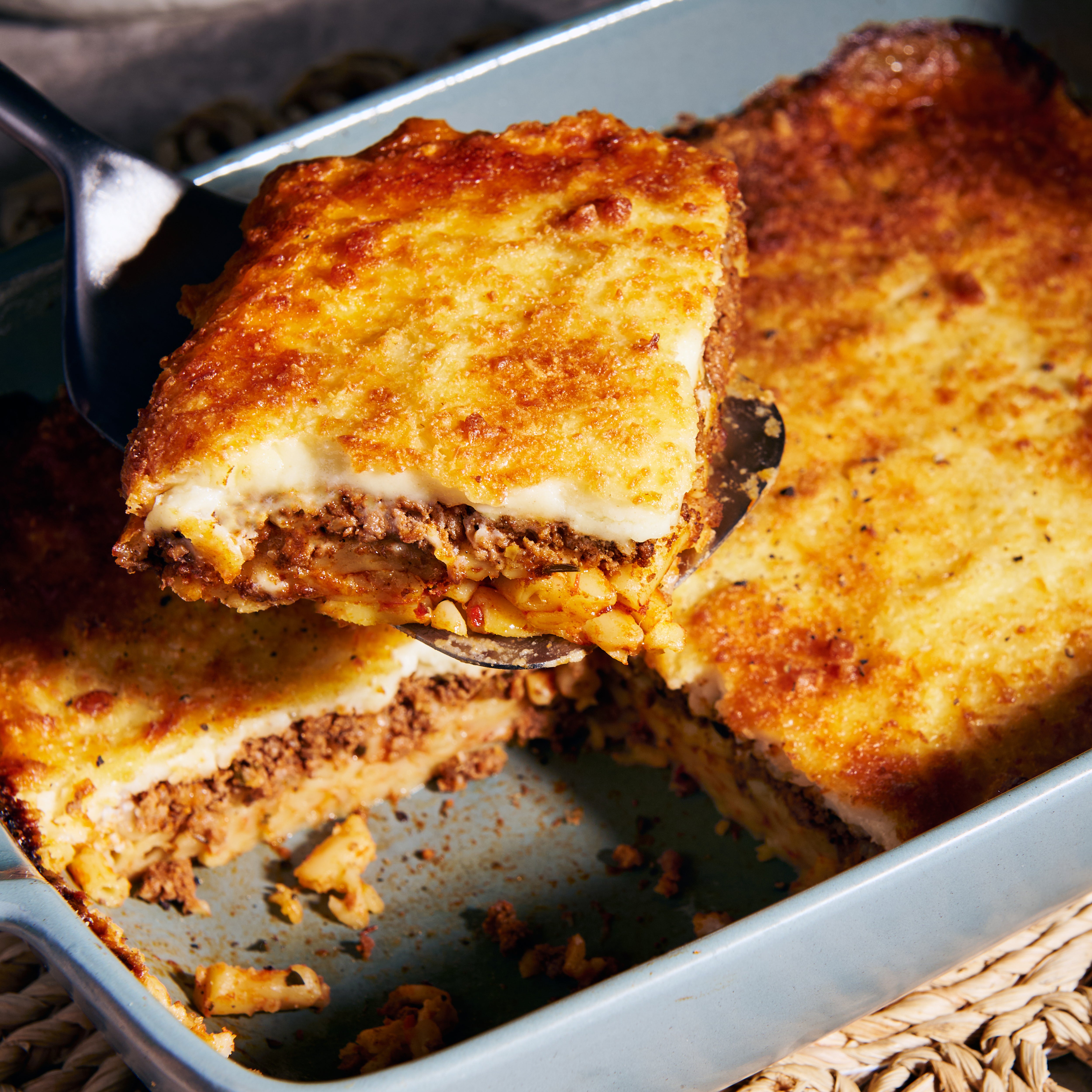Close-up of a spoon lifting a portion of lamb pastitsio, revealing the macaroni, lamb and creamy fetta bechemal layers
