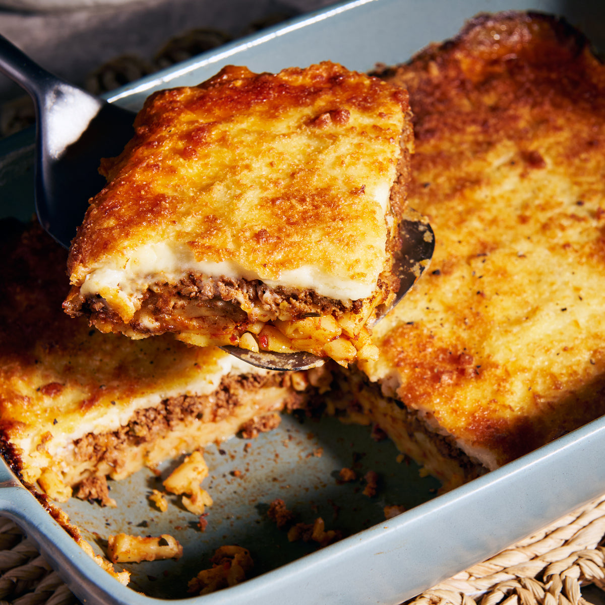 Close-up of a spoon lifting a portion of lamb pastitsio, revealing the macaroni, lamb and creamy fetta bechemal layers