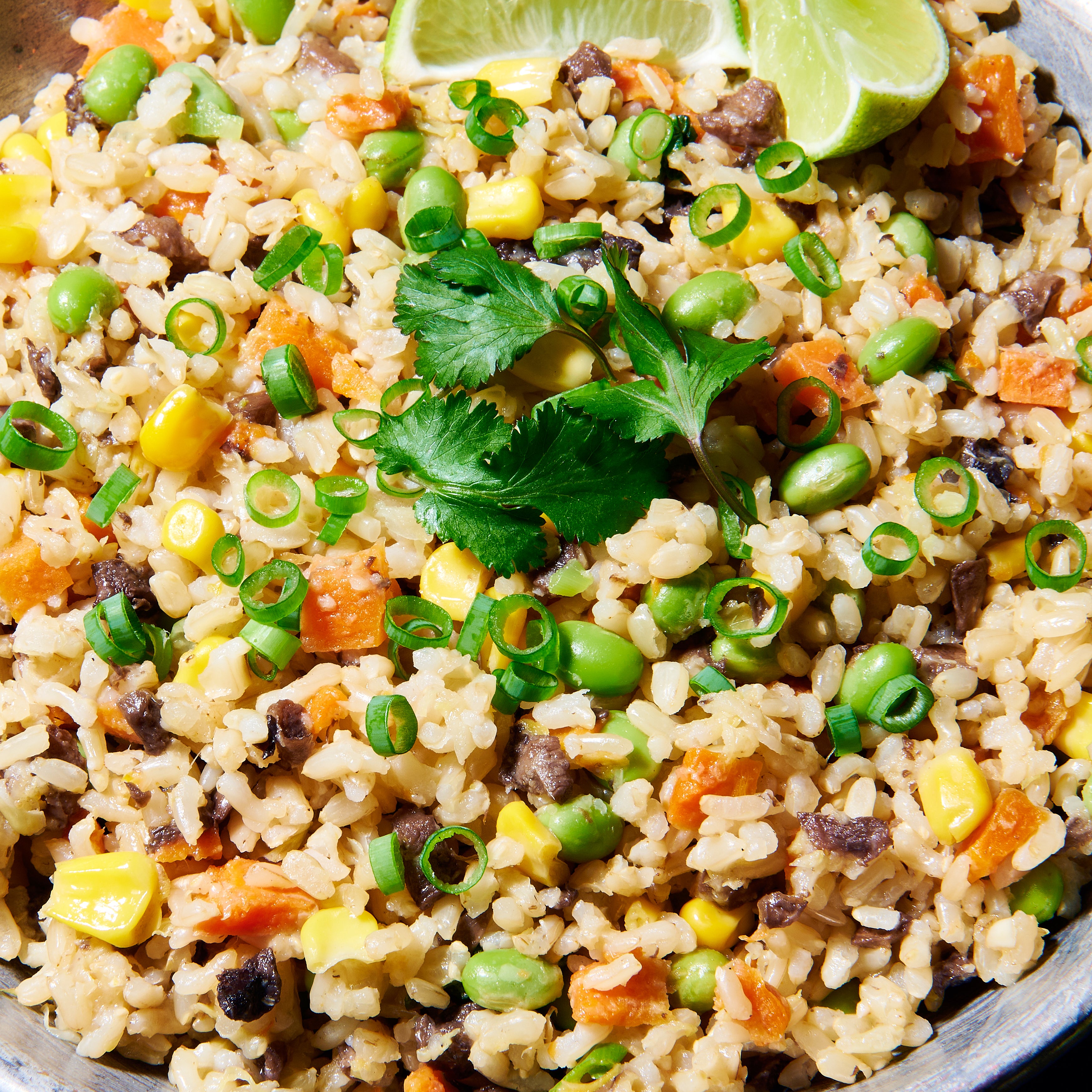 Close-up of super loaded vegie rice with brown rice, corn, edamame, mushrooms, and carrots, topped with coriander.