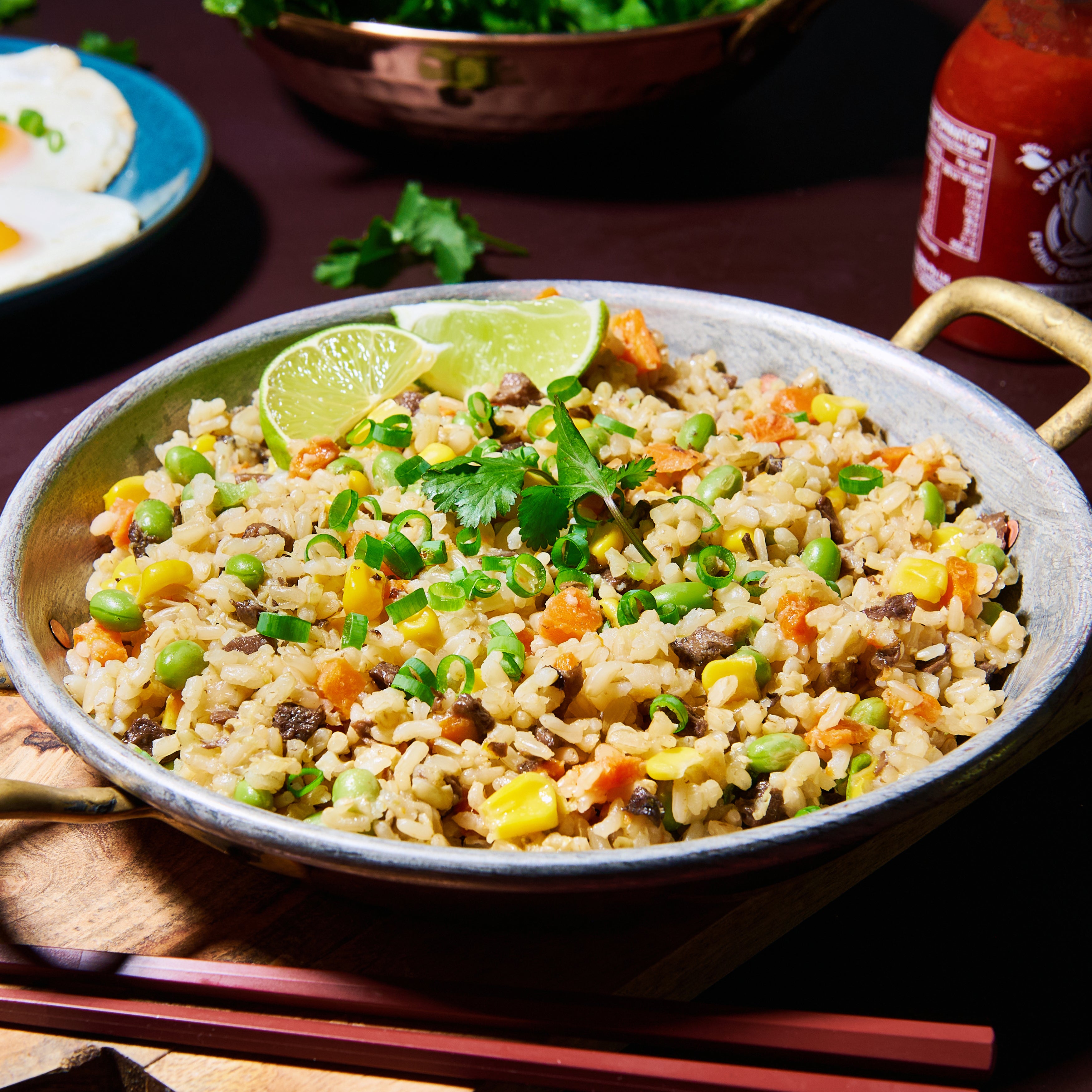 Overhead view of a pan filled with super loaded vegie rice, garnished with lime wedges and fresh coriander.