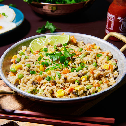Overhead view of a pan filled with super loaded vegie rice, garnished with lime wedges and fresh coriander.