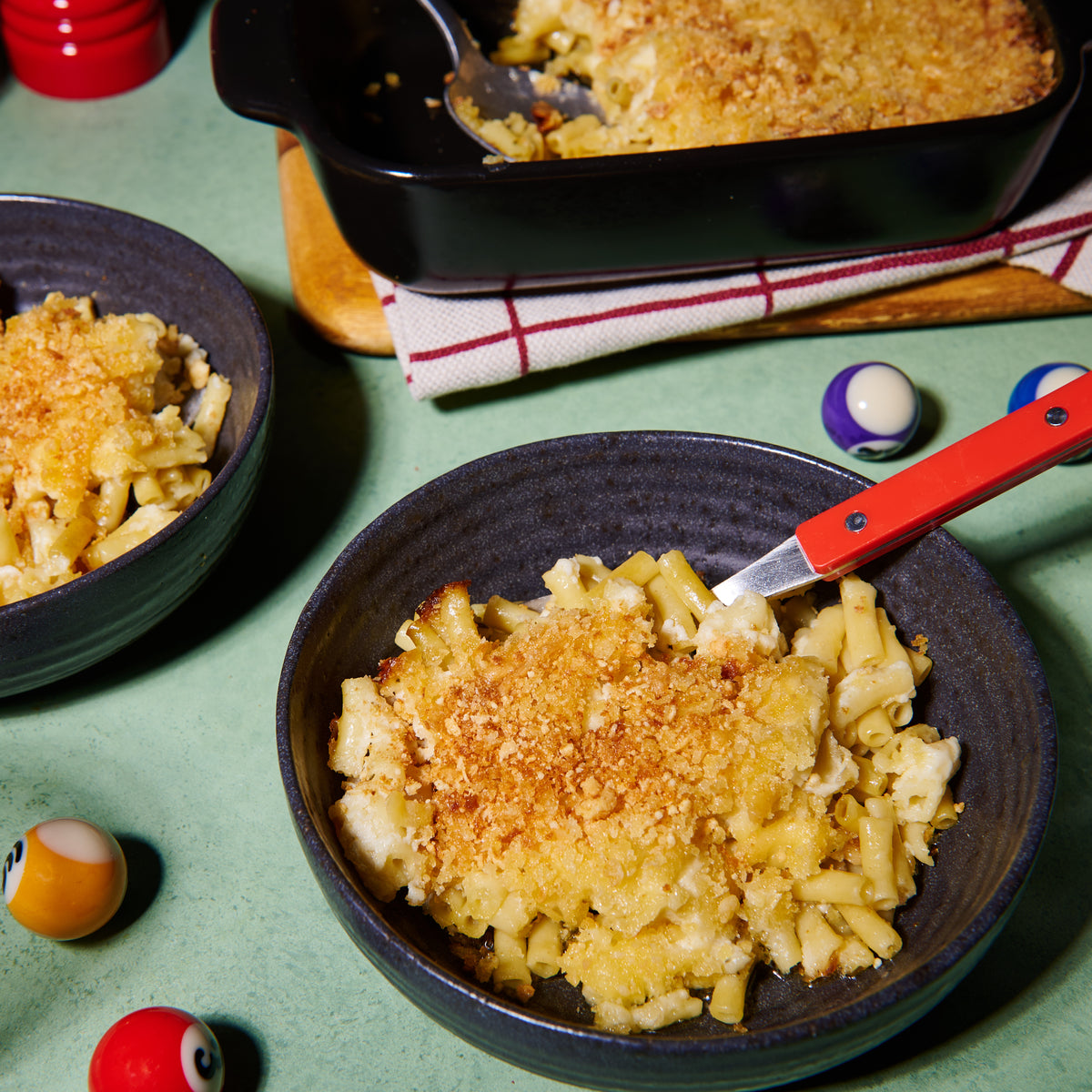 Two bowls of mac and cheese with a crunchy golden topping, served alongside a baking dish with the remainder of the pasta