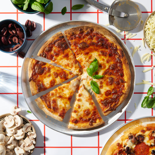 Overhead view of a sliced Margherita pizza on a metal tray, topped with melted mozzarella, tomato sauce, and fresh basil leaves.