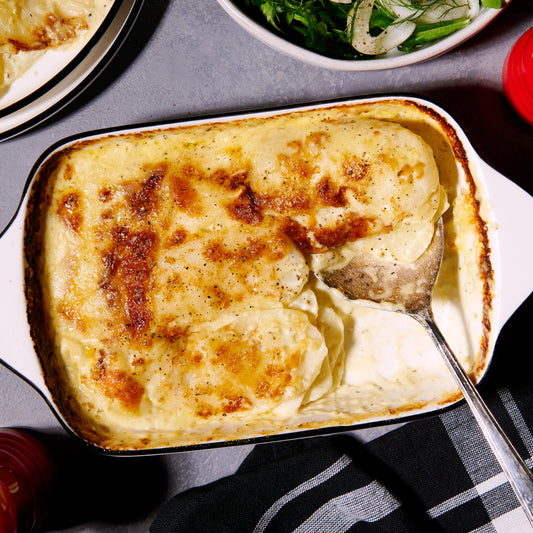Potato Gratin baked with thinly sliced potatoes in garlic-Parmesan cream, topped with golden Gruyere cheese, served in a baking dish with a portion taken out. Fennel and rocket salad on the side.