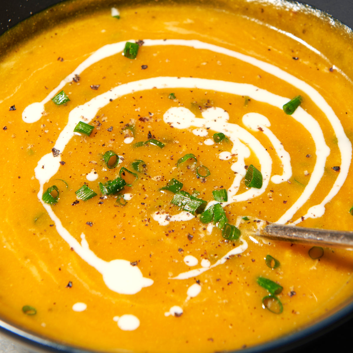 Pumpkin soup with roast garlic and thyme garnished with cream on top and sliced chives