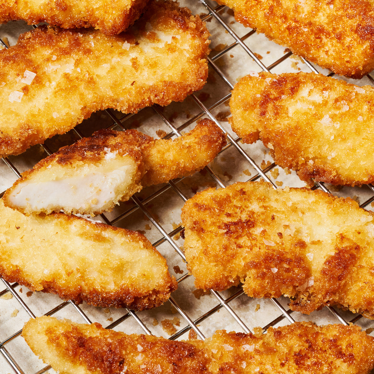 Close-up of panko-crusted chicken tenderloins on a cooling rack, showing the golden crumb coating and juicy interior