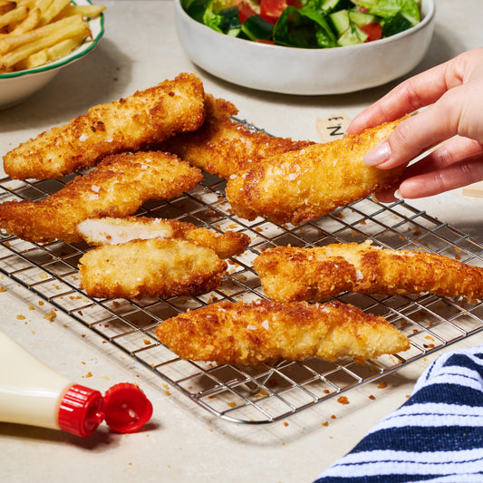 7 pieces of panko-crusted chicken tenderloins on a wire rack, served with chips and salad in the background