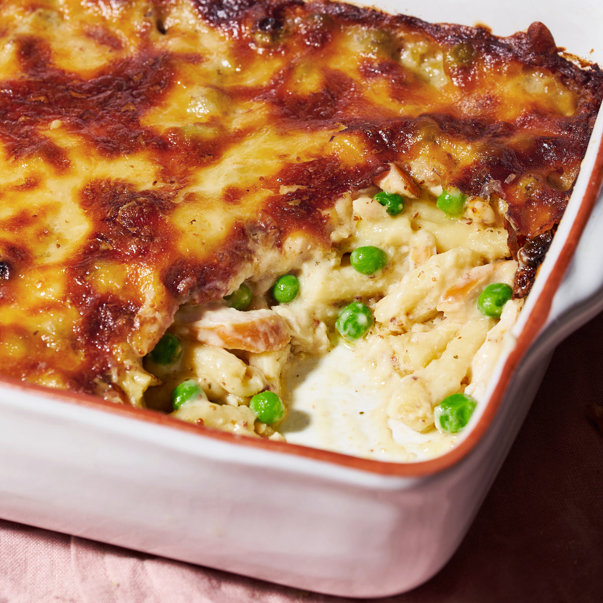 Close-up of smoked chicken pasta al forno, showing pasta, peas and shredded chicken in a creamy sauce beneath a golden baked cheese topping