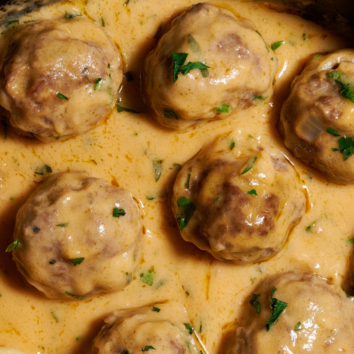 Close-up of Swedish meatballs in rich cream sauce, sprinkled with chopped parsley.