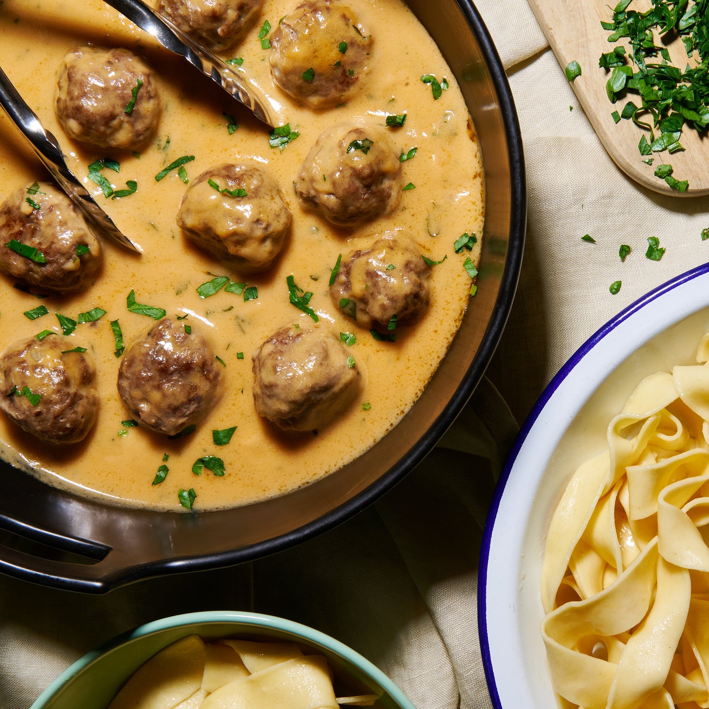 Overhead view of Swedish meatballs in creamy gravy, garnished with parsley, served in a pan with fresh pasta on the side.