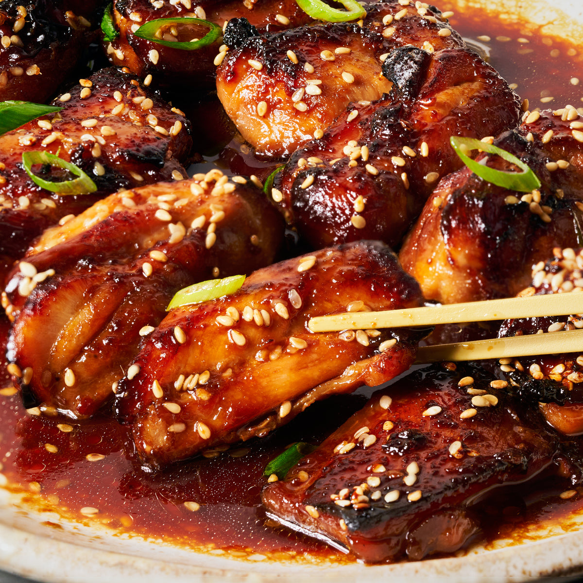 Close-up of teriyaki chicken glazed in a glossy sauce, topped with sesame seeds and spring onion