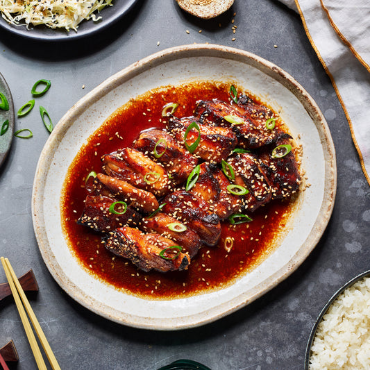 Teriyaki chicken in a glossy sauce, topped with sesame seeds and spring onion, served on a plate