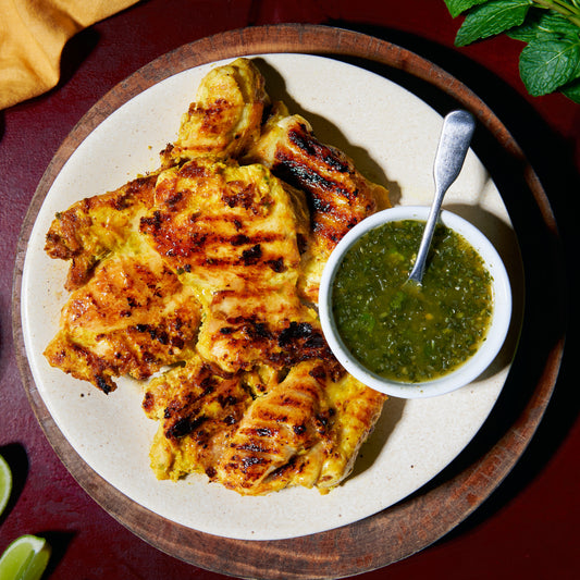 Four grilled turmeric chicken thighs, plated with a side of green chilli sauce