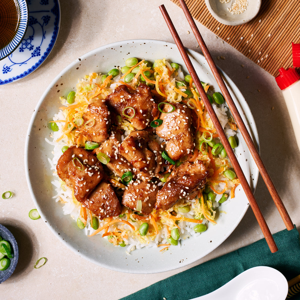 Teriyaki Chicken and Rice Bowl with glazed chicken, sushi rice, edamame & shredded carrots and cabbage, topped with roasted sesame seeds and sliced spring onion