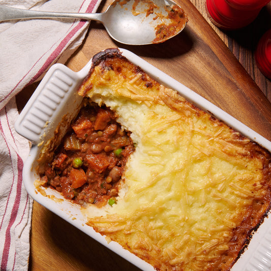 Vegetable cottage pie with cheesy potato mash with a portion scooped out to reveal a hearty borlotti bean and Puy lentil filling with carrot, celery and peas.