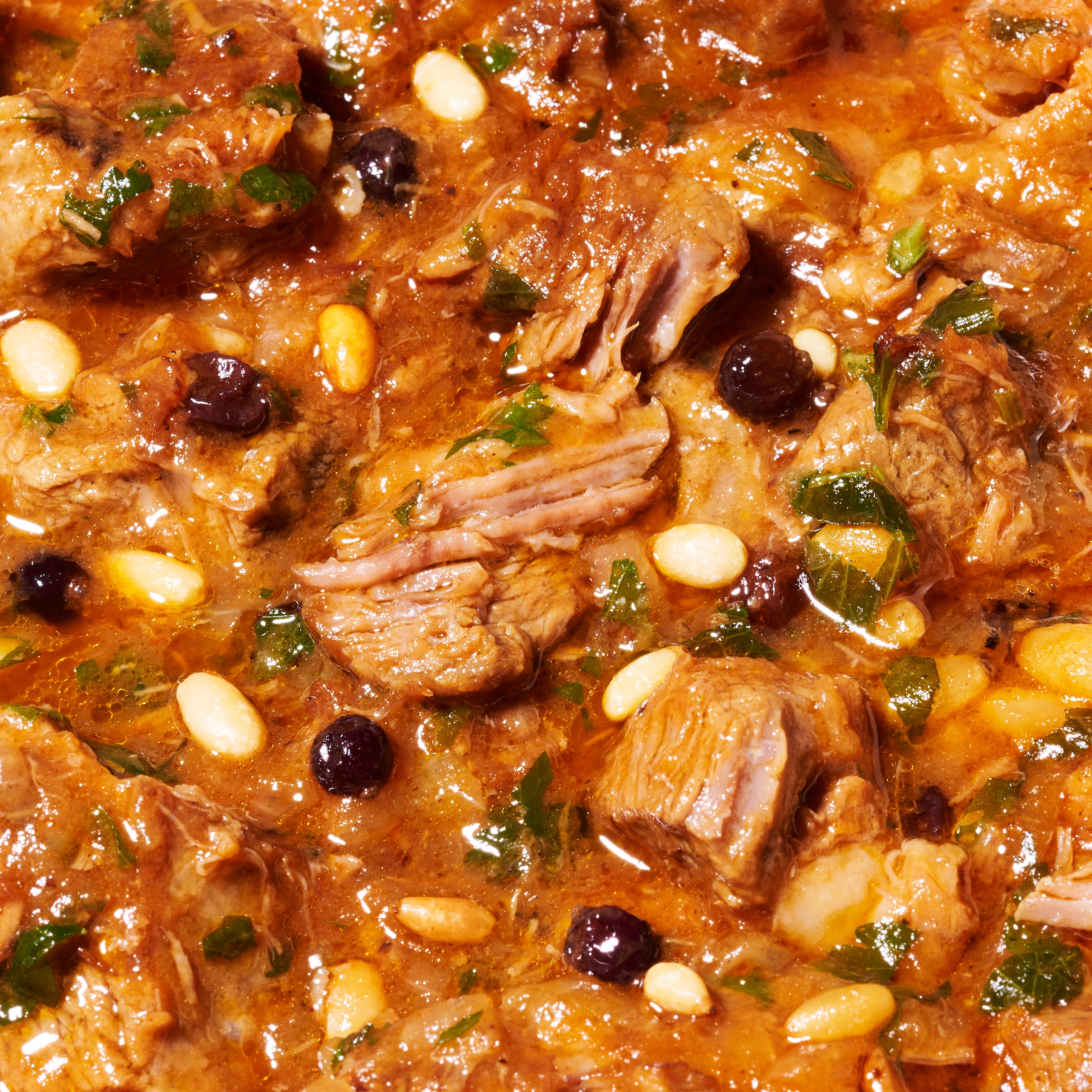 Close-up of slow-cooked lamb chunks in sweet and sour agrodolce sauce with pine nuts and currants.