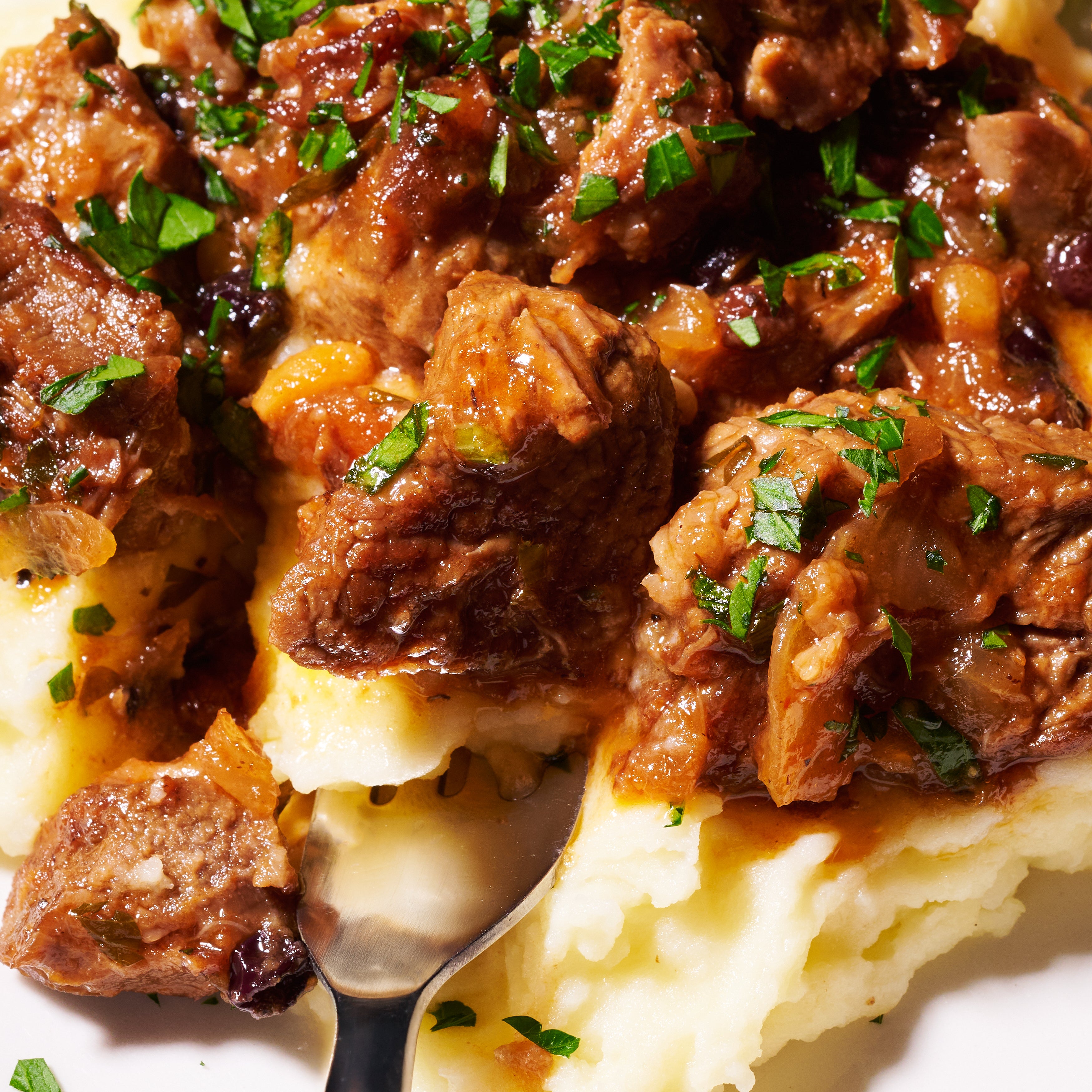 Close-up of forkful of tender agrodolce lamb on mashed potatoes, garnished with parsley.