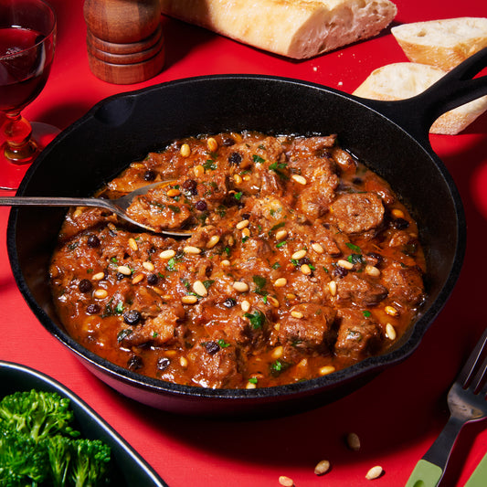 Skillet of agrodolce lamb stew with currants, pine nuts, and parsley in a rich tomato sauce.