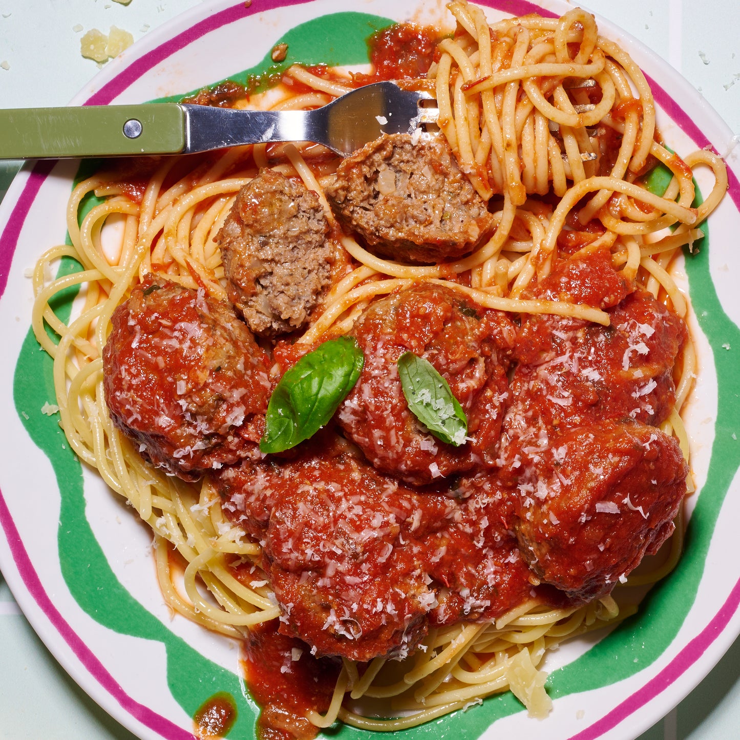 Plate of spaghetti topped with beefy Italian meatballs, tomato-basil sauce, grated Parmesan, and fresh basil.